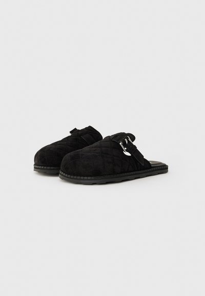 Black quilted slip-on slippers with adjustable side buckles and rubber soles on a plain light background.