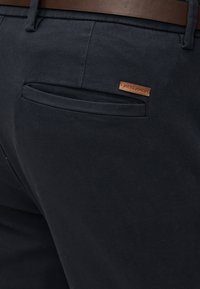 Μαύρο παντελόνι με τσέπη τύπου welt στο πίσω μέρος, που φέρει μια μικρή καφέ δερμάτινη ετικέτα με την επιγραφή "JACK & JONES" κάτω από μια καφέ ζώνη.