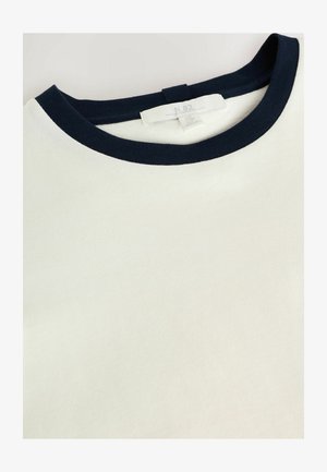 Puuvillane T-särk, millel on kreemjas keha ja tume tumesinine ribikrae. Sildilt leiab brändi ja hooldusjuhised. Sile tekstuur, lõdva stiiliga disain.