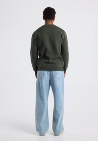 Green knit sweater with a round neckline, paired with light blue wide-leg jeans. The fabric appears soft with ribbed cuffs and hem.