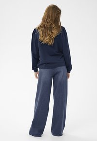 Marineblaue Sweatshirt mit Puffärmeln, kombiniert mit weit geschnittenen blauen Jeans. Glatte Textur, klare Linien und lässige Passform.