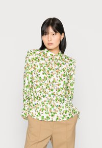 Blusa floral com fundo branco, apresentando flores verdes, azuis e bege. Tem gola alta e mangas longas com punhos abotoados.