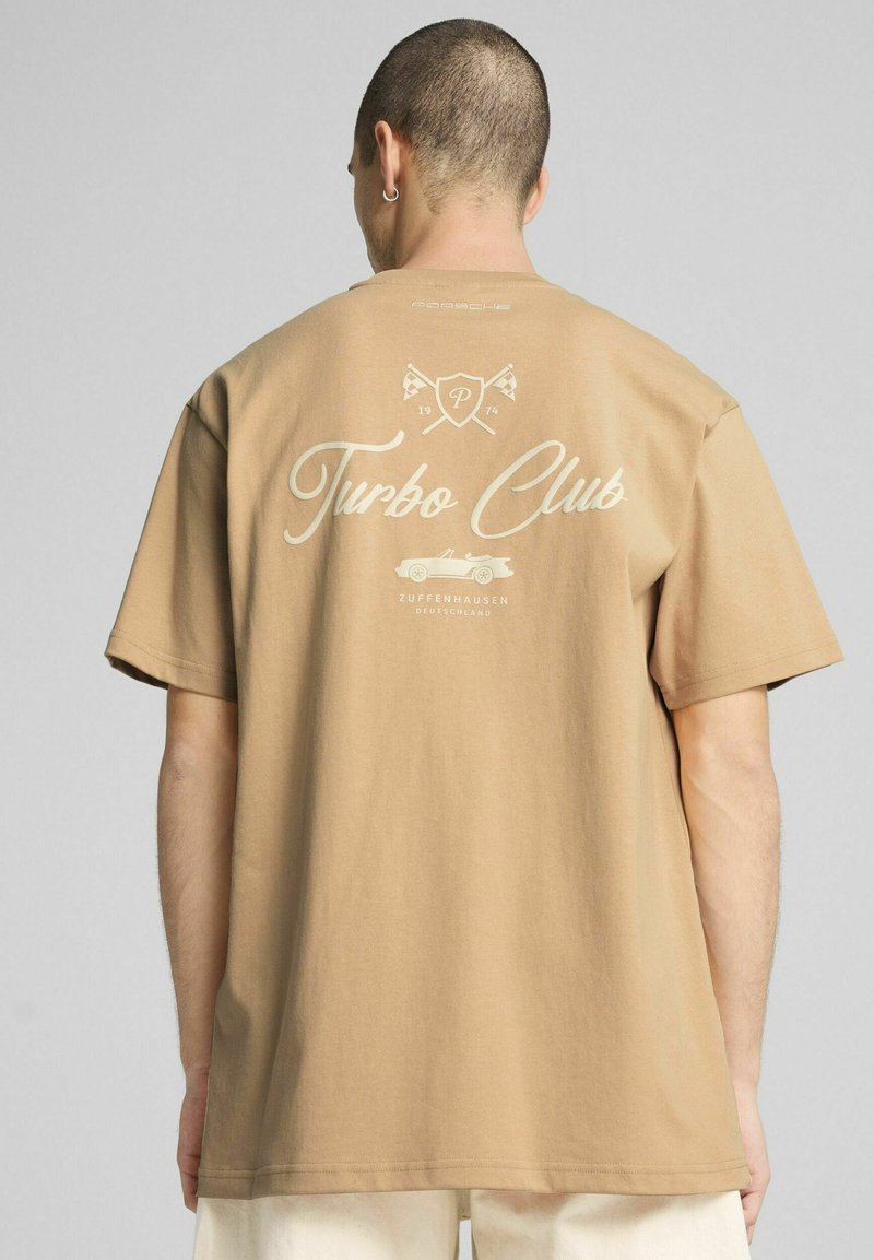 Sandfarvet bomulds-T-shirt med løs pasform. Har et trykt "Turbo Club" logo og grafik på ryggen. Korte ærmer og rund halsudskæring.