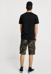Svart t-skjorte med korte ermer kombinert med grønne camo cargo shorts med flere lommer, båret med svarte høye sneakers.