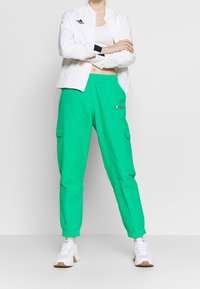 Zielone spodnie cargo z elastycznymi mankietami, wyposażone w boczne kieszenie i małe logo. Połączone z białą kurtką zapinaną na zamek i białymi trampkami.
