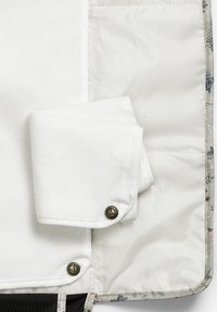 Kangaslaukun sisäosa, jossa on valkoinen taiteltu pyyhe, joka on kiinnitetty nepparilla. Pehmeä rakenne, neutraalit värit ja kuvioitu reuna.