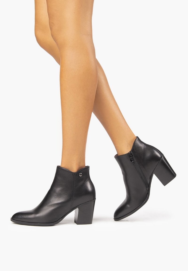 Bottes basses en cuir noir avec un talon bloc de hauteur moyenne, un bout pointu, une fermeture éclair latérale et une texture lisse. Conçues avec un accent de logo subtil.