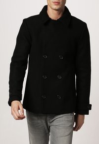 Černý vlněný kabát peacoat s dvouřadým designem, velkým límcem a černými knoflíky. Má přiléhavý siluetu a texturovanou tkaninu.
