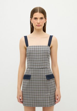 Ruudullinen mekko, jossa on neliskulmainen pääntie, leveät farkkuolkaimet ja etutaskut. Valmainen vaaleanbeige ja laivastonsininen väri, istuva malli.