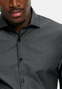 Dunkelgraues Hemd mit subtilen Punkten, im Button-Down-Stil und aus strukturiertem Stoff. Verfügt über schwarze Knöpfe auf der Vorderseite.