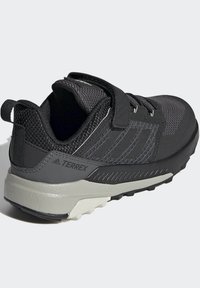 Černé sportovní boty s texturovaným svrškem, nastavitelným páskem a gumovou podrážkou. Obsahují šedé akcenty a zesílenou oblast paty.