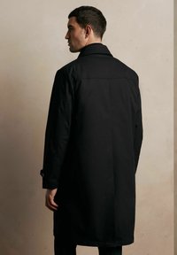 Czarny płaszcz trenchowy o gładkiej fakturze, z długimi rękawami i zapięciem na guziki. Zaprojektowany z dopasowanym krojem i rozcięciem z tyłu dla lepszej funkcjonalności.