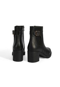 Schwarze Leder-Stiefeletten mit einem stabilen Absatz, ausgestattet mit seitlichen elastischen Einsätzen und einer dekorativen Schnalle. Glatte Textur und minimalistisches Design.