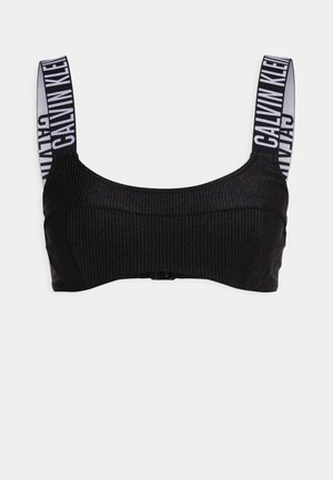 Black ribbed bralette with wide straps featuring white "CALVIN KLEIN" branding. Simple design, soft texture, and hook closure at the back.