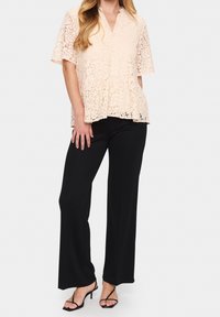 Peach lace top with short sleeves and a v-neckline, worn with black wide-leg pants and black strappy heeled sandals.