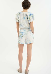 Blusa corta de manga corta con estampados en azul y verde, combinada con pantalones cortos florales. Tejido ligero y corte relajado. Se muestra vista trasera.