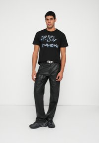 Μαύρο γραφικό μπλουζάκι με μπλε κείμενο, συνδυασμένο με μαύρο δερμάτινο παντελόνι cargo με φερμουάρ στις τσέπες και υφασμένη υφή. Μαύρα αθλητικά παπούτσια.