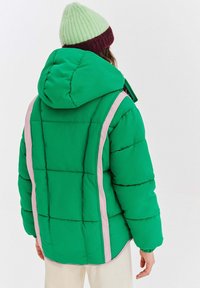 Zelená páperová bunda s rebrovanou textúrou, s ružovým pruhom na boku a kapucňou. Viditeľné prešívanie poskytuje štruktúrovaný tvar a izoláciu.