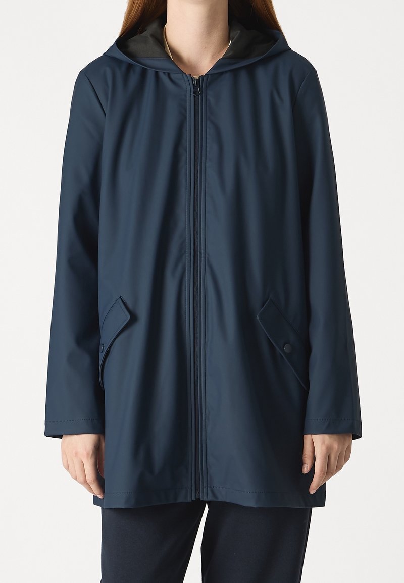 Marinblå vattentät jacka med dragkedja fram, huva och två sidofickor. Har en slät yta och en avslappnad passform.