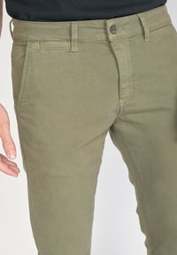 Pantalon en coton couleur kaki avec une coupe slim, doté d'une fermeture éclair, d'un bouton et de poches standard. Détails de couture subtils sur l'ensemble.