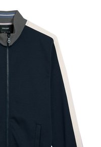 Giacca a zip blu navy con strisce laterali crema, colletto grigio e tessuto testurizzato. Presenta una tasca frontale e polsini a coste.