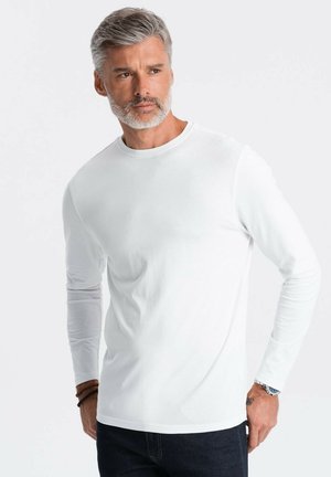 Camiseta de manga larga blanca hecha de algodón suave. Presenta un cuello redondo y un ajuste ceñido. Combinada con unos jeans de mezclilla oscura.