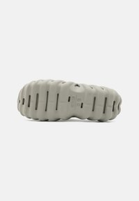 Gray rubber shoe with a contoured, wavy design. Features cut-out segments for ventilation. Textured surface with branding detail.