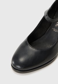 Schwarzer Lederschuh mit abgerundetem Zehenbereich und einem Knöchelriemen. Glatte Oberfläche, minimalistisches Design und ein niedriger Absatz für Stabilität.