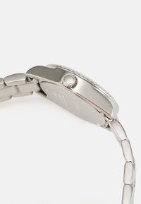 Silver stainless steel watch with a round case, textured bezel, and a smooth finish. Features a simple crown and linked bracelet design.
