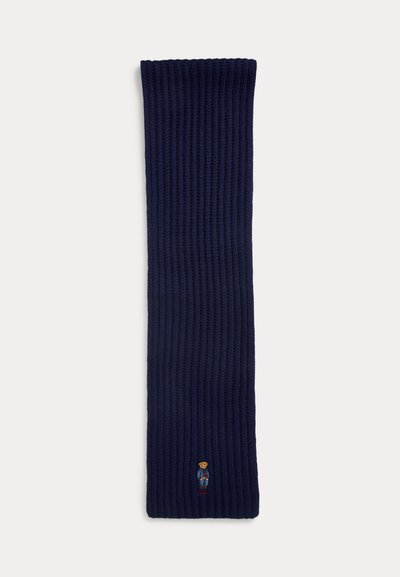 Fular tricotat în relief, de culoare bleumarin, cu un mic logo cu urs brodat aproape de partea de jos. Textură moale, cu o formă largă, dreptunghiulară.
