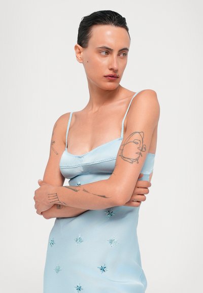 Vestido de satén azul claro con tirantes finos, que presenta motivos de estrellas bordados en diferentes tonos de azul y una silueta ajustada.