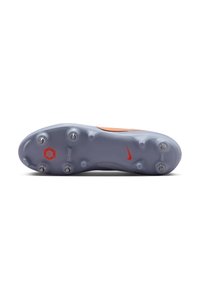 Semelle de chaussure de soccer gris clair avec sept crampons métalliques, un petit logo Nike rouge et un emblème hexagonal orange près de la zone des orteils.