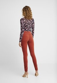 Högmidjade, rostfärgade kordbyxor med två bakfickor, ihopparade med en långärmad svart blommig topp med rosa och vita mönster.