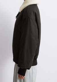 Svart bomberjacka med en mysig vit fleecekrage, ribbade ärmslut, sidofickor och en slät, matt finish. Skräddarsydd passform.