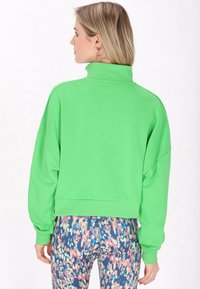 Zöld, rövidított pulóver magas gallérral és laza ujjakra, kék, rózsaszín és krém árnyalatú mintás leggingsszel párosítva.