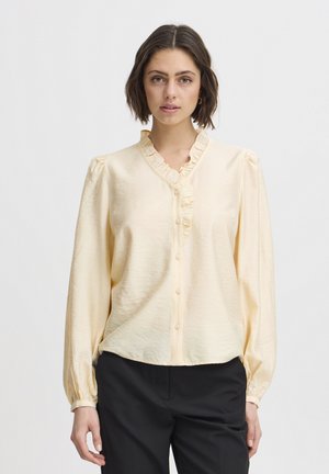 Cremfarbene Bluse aus glattem Stoff mit Rüschkragen und Knopfverschluss. Hat lange Ärmel mit gerafften Manschetten und eine lockere Passform.