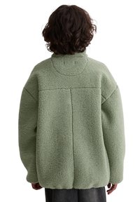 Zielona bluza polarowa z wysokim kołnierzem; luźny fason; teksturowana, miękka tkanina; widoczne szwy z tyłu.