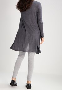 Tunica lunga grigio scuro con orlo dritto e spacchi laterali, abbinata a leggings grigio chiaro e scarpe nere flat. Tessuto morbido, vestibilità rilassata.