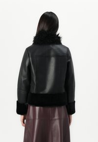 Veste en cuir noir avec un col et des poignets en fausse fourrure. Présente un design ajusté avec une texture lisse et une longueur courte.