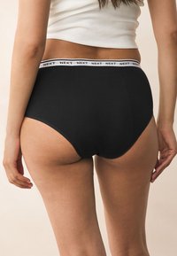 Culottes en coton noir avec une ceinture élastique blanche imprimée de la marque "NEXT". Texture lisse avec un design classique taille haute.