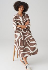 Brown and white patterned midi dress with a button-up front, long sleeves, flared skirt, and gathered hem, paired with casual sneakers.