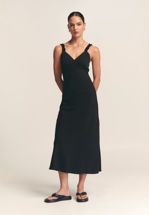 Black midi dress with ruffled straps, fitted bodice, and flared hem. Paired with black flat sandals. Smooth, lightweight fabric.