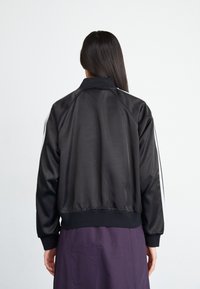 Black satin bomber jacket with a ribbed hem and cuffs, featuring white side stripes. The design is relaxed fit with a classic collar.