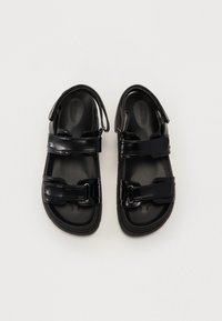 Sandalias negras con correas ajustables, hechas de material sintético brillante, con una suela resistente y una textura suave.