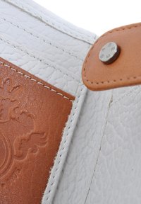 Witte gestructureerde leer met een gladde bruine leren accenten, voorzien van witte stiksels en een zilveren metalen drukknoopdetail.