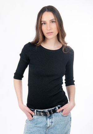 Sort, ribbet langærmet top med rund halsudskæring, båret med et lyseblåt denimskørt. Modellen har et sort bælte med sølvfarvede beslag.