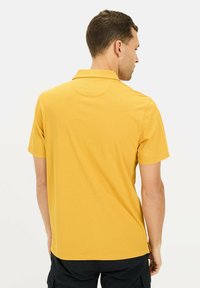 Koszulka polo z krótkim rękawem w teksturowanym żółtym materiale, z kołnierzykiem i detalem na karku, w połączeniu z czarnymi szortami cargo.