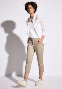 Lekka, biała bluzka w stylu eyelet na białym topie na ramiączkach, w zestawieniu z beżowymi spodniami typu cropped i białymi trampkami z szarymi akcentami.