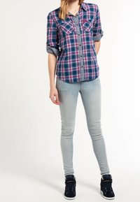 Rutigt button-up skjorta i marinblått, rosa och vitt med uppvuxna ärmar, i kombination med ljusblå skinny jeans och svarta högstövlar.