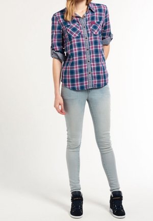 Chemise à carreaux bleu marine, rose et blanc avec des manches retroussées, associée à un jean skinny bleu clair et des baskets montantes noires.